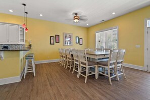 A dining area with a wooden table and chairs, a kitchen with white cabinets, and a ceiling fan.