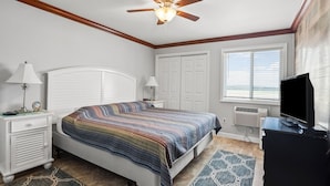 A bedroom with a bed, nightstands, a ceiling fan, a TV, and a window with blinds. - Best panoramic views in NMB! Views of inlet, across street from beach, pool, tennis, fish, surf (North Myrtle Beach)