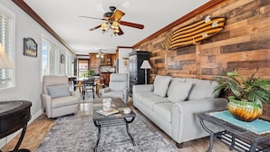 A spacious living room with a gray sofa, a coffee table, and a dining area with wooden cabinets. - Best panoramic views in NMB! Views of inlet, across street from beach, pool, tennis, fish, surf (North Myrtle Beach)