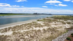 A coastal landscape with a beach, dunes, and a distant tree line. - Best panoramic views in NMB! Views of inlet, across street from beach, pool, tennis, fish, surf (North Myrtle Beach)