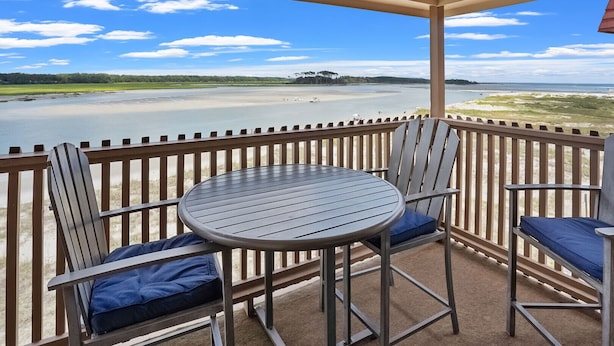 A balcony with a round table and four chairs, overlooking a beach and water. - Best panoramic views in NMB! Views of inlet, across street from beach, pool, tennis, fish, surf (North Myrtle Beach)