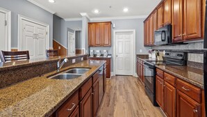 A modern kitchen with granite countertops, wooden cabinets, a stainless steel sink, and a black stove. - Large villa just steps to the beach w/private pool, game room & elevator-perfect family rental (North Myrtle Beach)