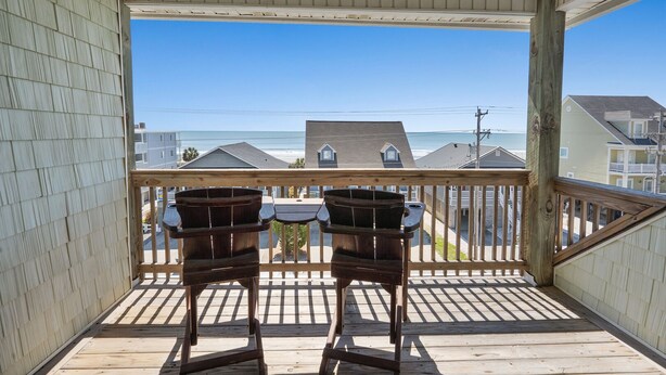 A wooden deck with two chairs facing a view of the beach and houses. - Large villa just steps to the beach w/private pool, game room & elevator-perfect family rental (North Myrtle Beach)