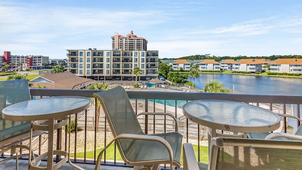 A balcony with outdoor seating, overlooking a body of water and a building complex.