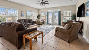 A spacious living room with a large sofa, a smaller armchair, a coffee table, and a ceiling fan. - Beautiful villa w/private pool, hot tub & game room-grill & picnic table-in North Myrtle Beach (North Myrtle Beach)