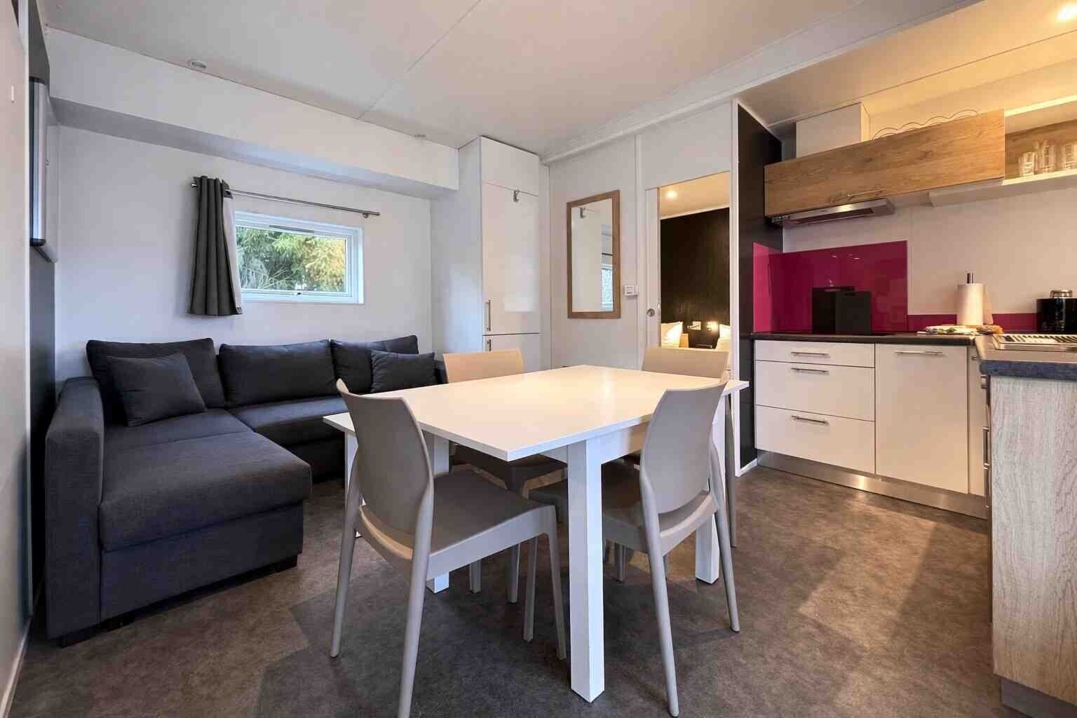A compact living space with a sofa, dining table, chairs, kitchenette, and a window with curtains.