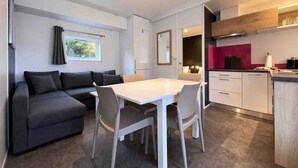 A compact living space with a sofa, dining table, chairs, kitchenette, and a window with curtains.