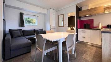 A compact living space with a sofa, dining table, chairs, kitchenette, and a window with curtains.