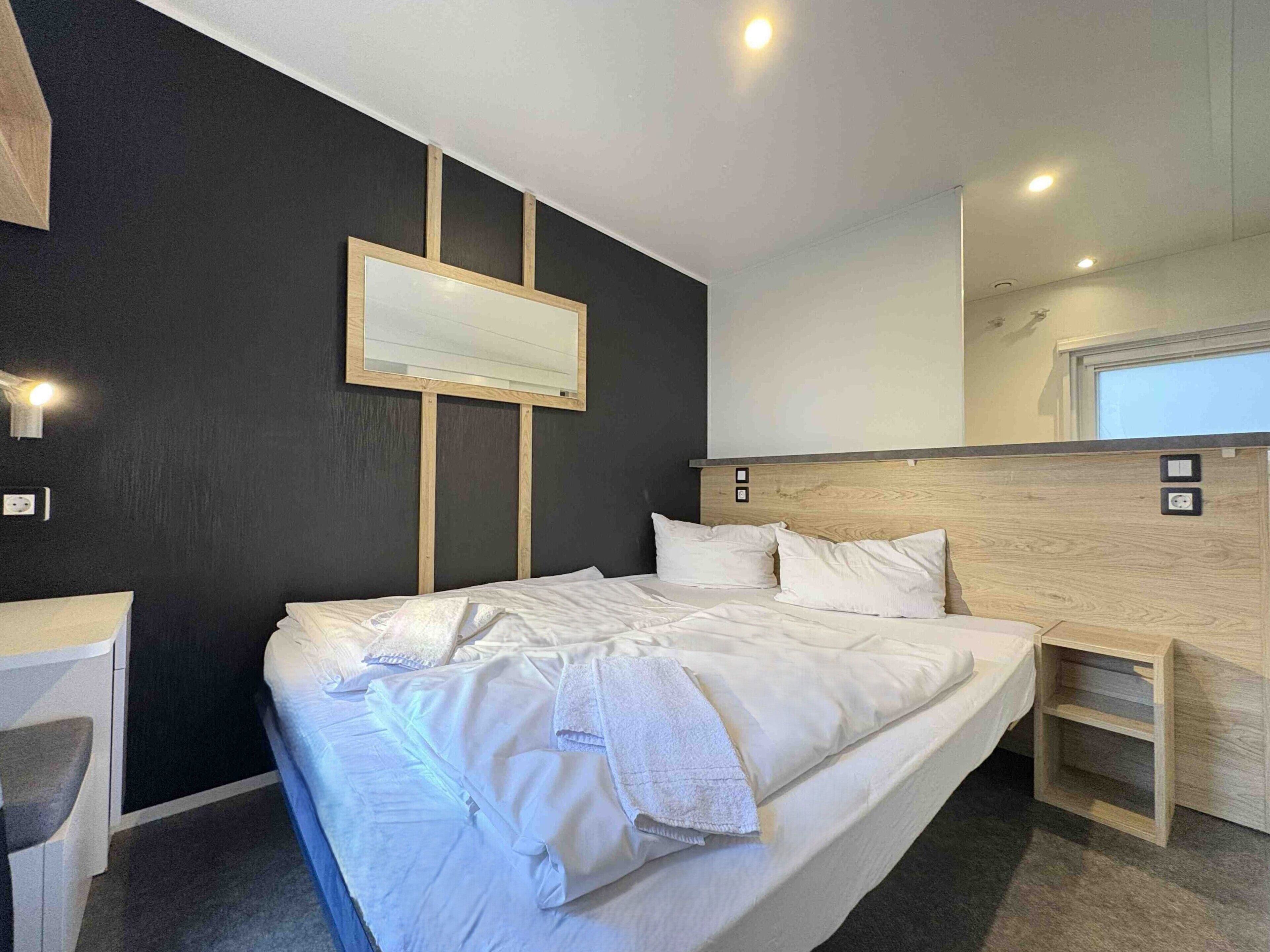Une chambre d’hôtel moderne avec un grand lit, des tables de chevet, un miroir et un téléviseur fixé au mur.