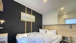 A modern hotel room with a large bed, bedside tables, a mirror, and a wall-mounted TV.