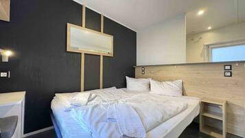 A modern hotel room with a large bed, bedside tables, a mirror, and a wall-mounted TV.