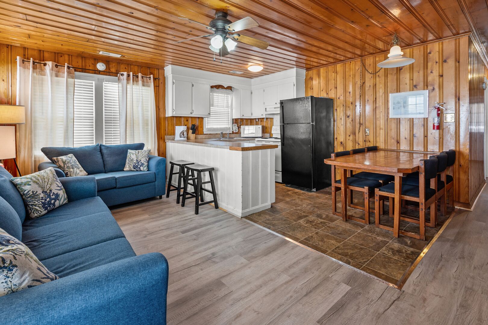 L'intérieur d'un chalet accueillant, avec un canapé bleu, une table à manger en bois et un coin cuisine.