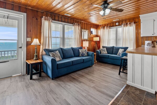 A cozy living room with two blue sofas, a wooden ceiling, and a view of the ocean through the windows. - Beautiful oceanfront balcony at this pet-friendly, cozy apartment steps from the sand (North Myrtle Beach)