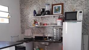 Een kleine keuken met een gasfornuis, een koelkast, een magnetron en een gasfles.