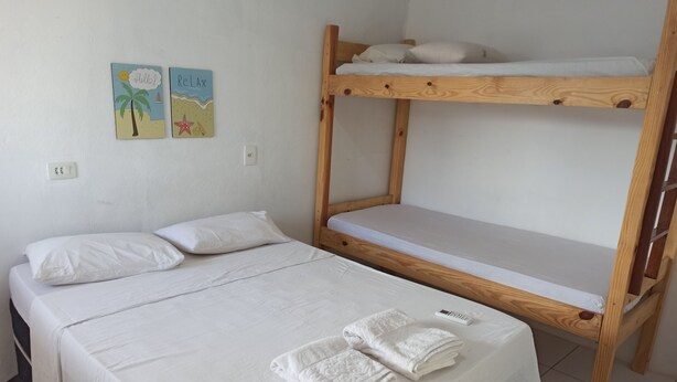 Een kamer met een stapelbed en een enkel bed, beide met wit beddengoed. Twee decoraties aan de muur, één met een palmboom en de ander met een zeester.
