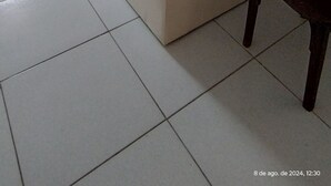 Een woonkamer met een beige bank, een houten stoel en een raam met gordijnen.