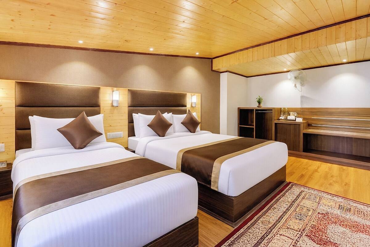 A hotel room with two beds, wooden paneling, a small desk, and a plant.