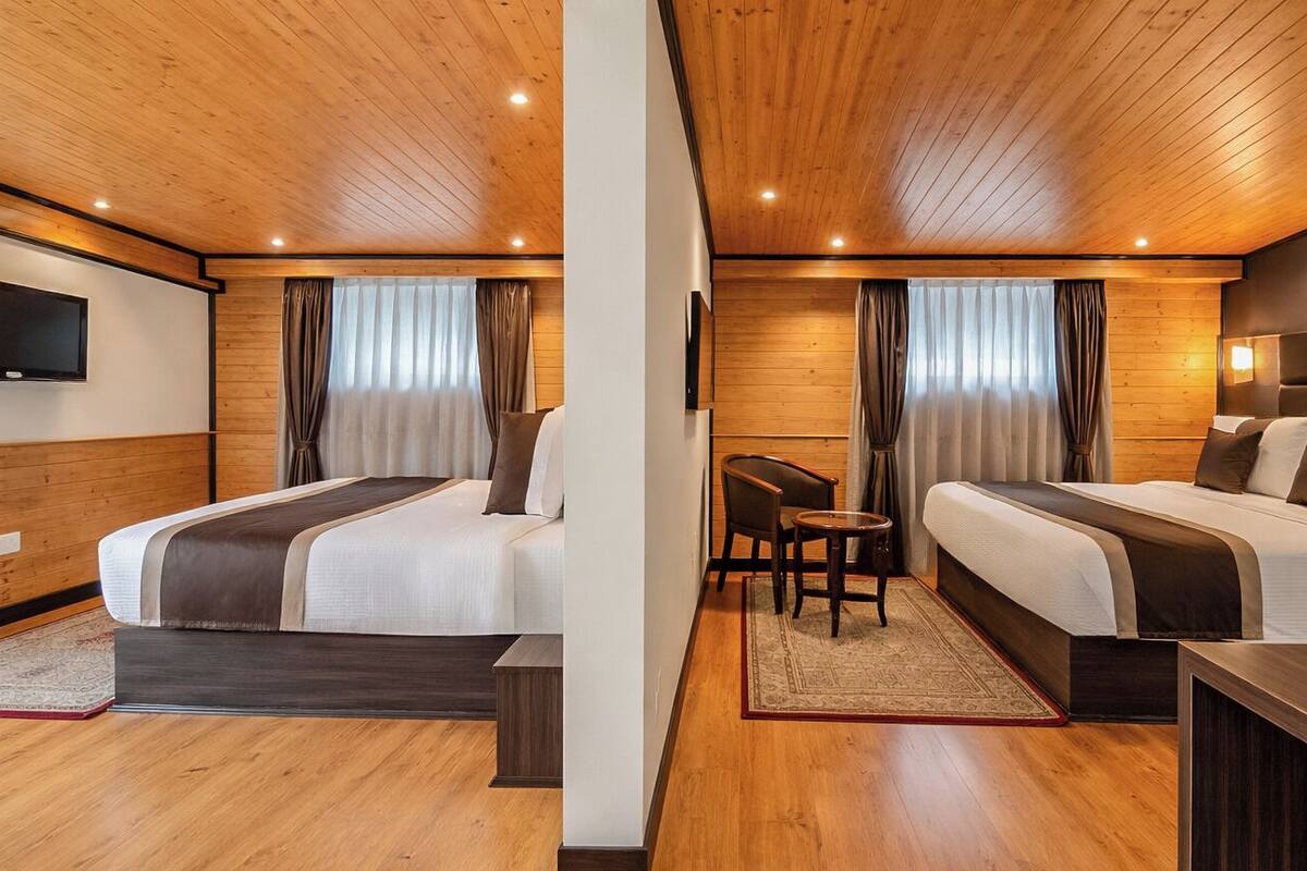 A hotel room with wooden ceilings, two beds, a TV, a small table, and a chair.