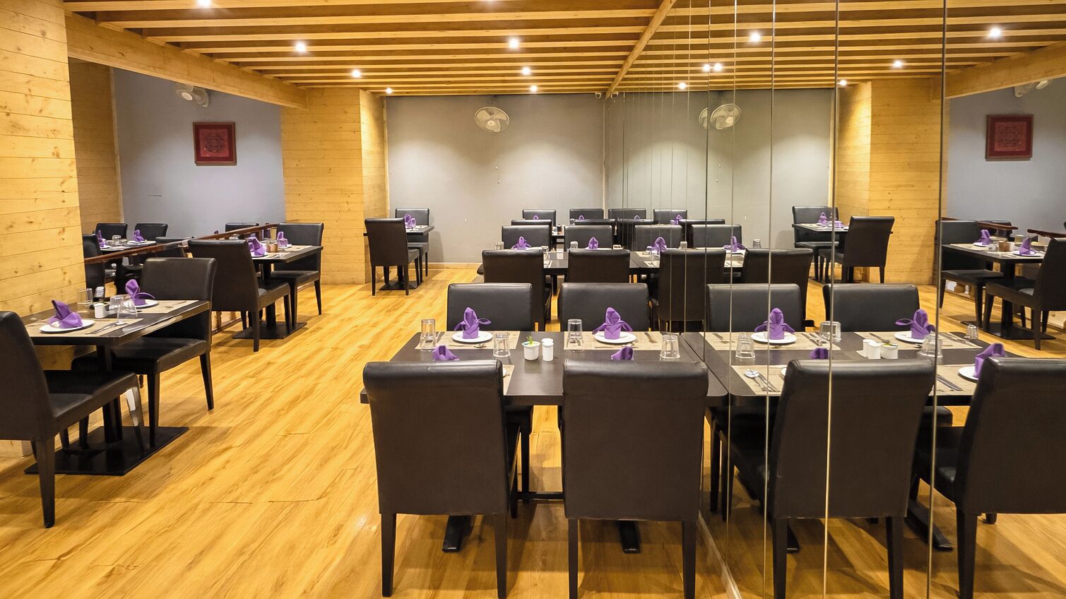 A conference room with multiple tables and chairs, wooden floors, and ceiling fans.