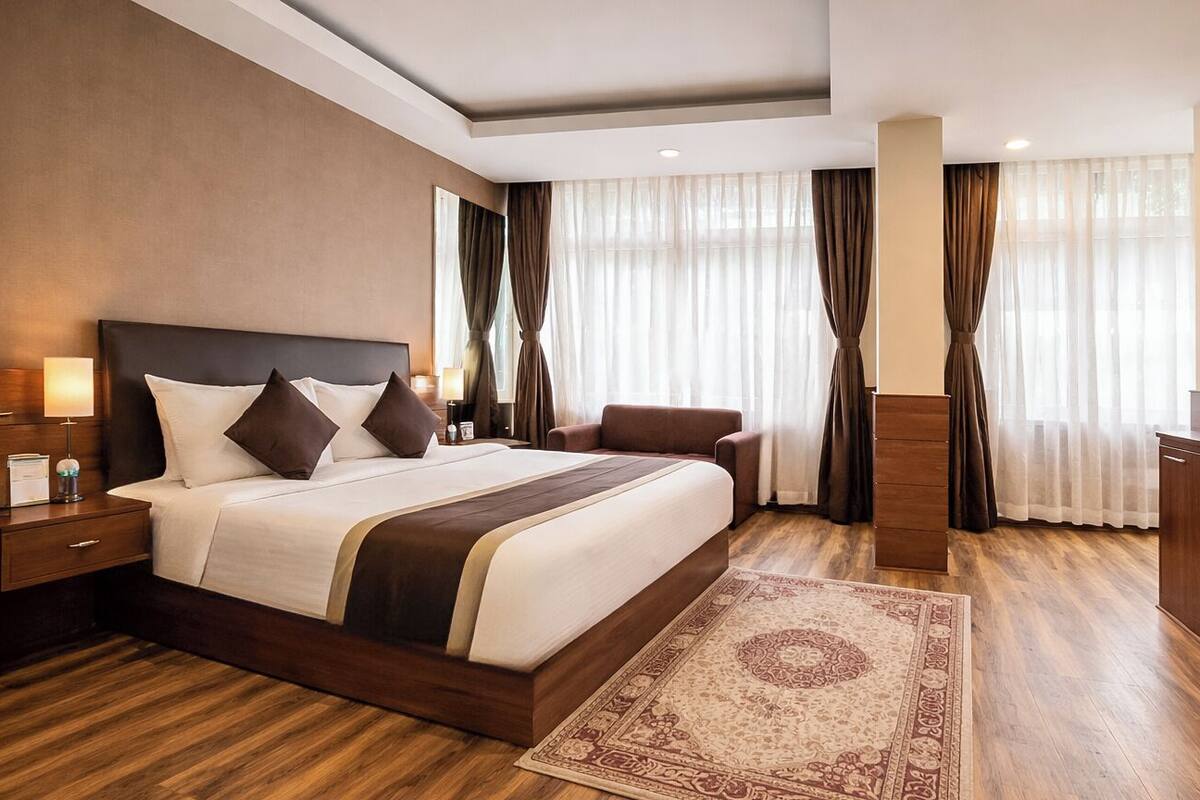 A hotel room with a large bed, a desk, a chair, a nightstand, and a rug.