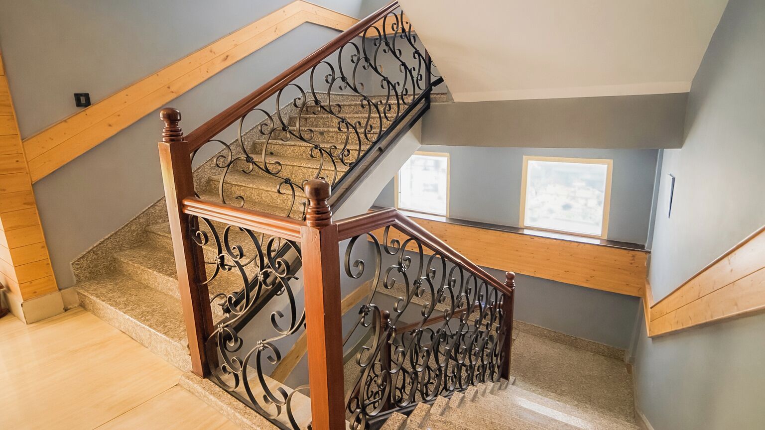 Eine hölzerne Treppe mit aufwendiger Metallreling, Teppichstufen und Blick auf die obere Etage.