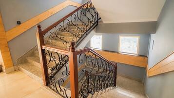 Eine hölzerne Treppe mit aufwendiger Metallreling, Teppichstufen und Blick auf die obere Etage.