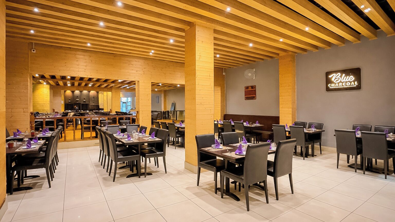 A restaurant with wooden ceiling beams, tables with purple napkins, and a sign reading 'Blue Coast Restaurant.'