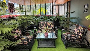 An indoor garden with a glass table, black wicker chairs with floral upholstery, and various potted plants. - Sumitel Shangrila (Gangtok)