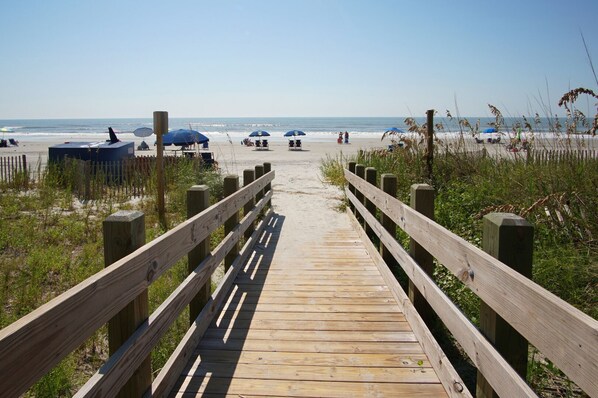 A wooden boardwalk leading to a beach with umbrellas and beach chairs.