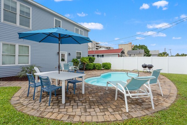 A backyard with a swimming pool, patio furniture, and a barbecue grill.