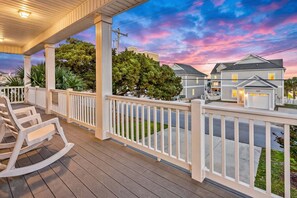 A wooden porch with white railings, a view of a residential street, and a sunset sky.