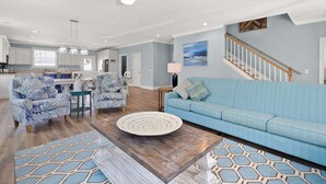 Ein geräumiger Wohnbereich mit einem blauen Sofa, gemusterten Sesseln, einem Couchtisch und einer Treppe, die zu einer oberen Etage führt.