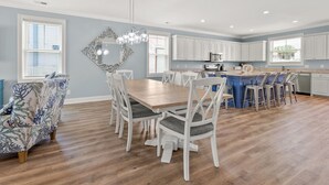 Eine moderne Küche mit weißen Schränken, einer blauen Kücheninsel und einem Essbereich mit Holztisch und weißen Stühlen.