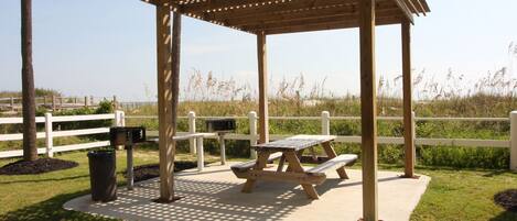 A wooden gazebo with a lattice roof, picnic tables, and a white fence in the background.