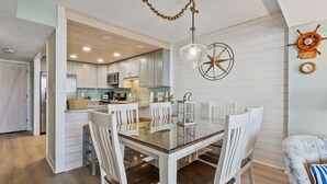 Una cocina moderna con armarios blancos, una mesa de comedor con sillas blancas y una lámpara colgante.
