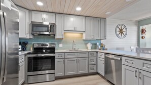 Una cocina moderna con electrodomésticos de acero inoxidable, gabinetes grises y techo de madera.