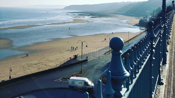 A coastal road with a beach in the background, a white van, and a decorative railing.