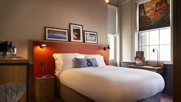 A neatly arranged hotel room with a large bed, a bedside table with a lamp, a chair, and a window with a view.