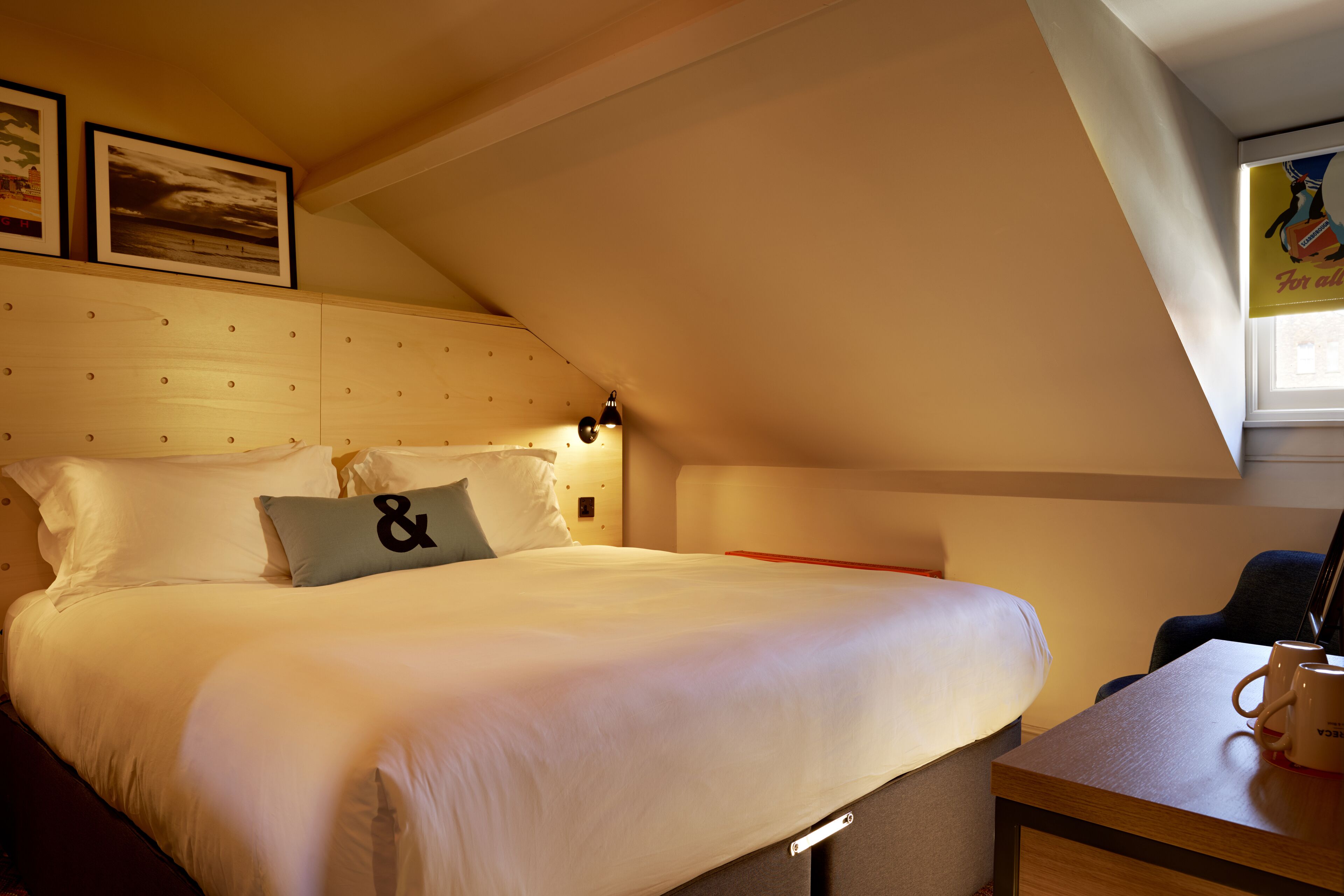 A neatly made bed with white linens and a pillow with a large ampersand symbol.