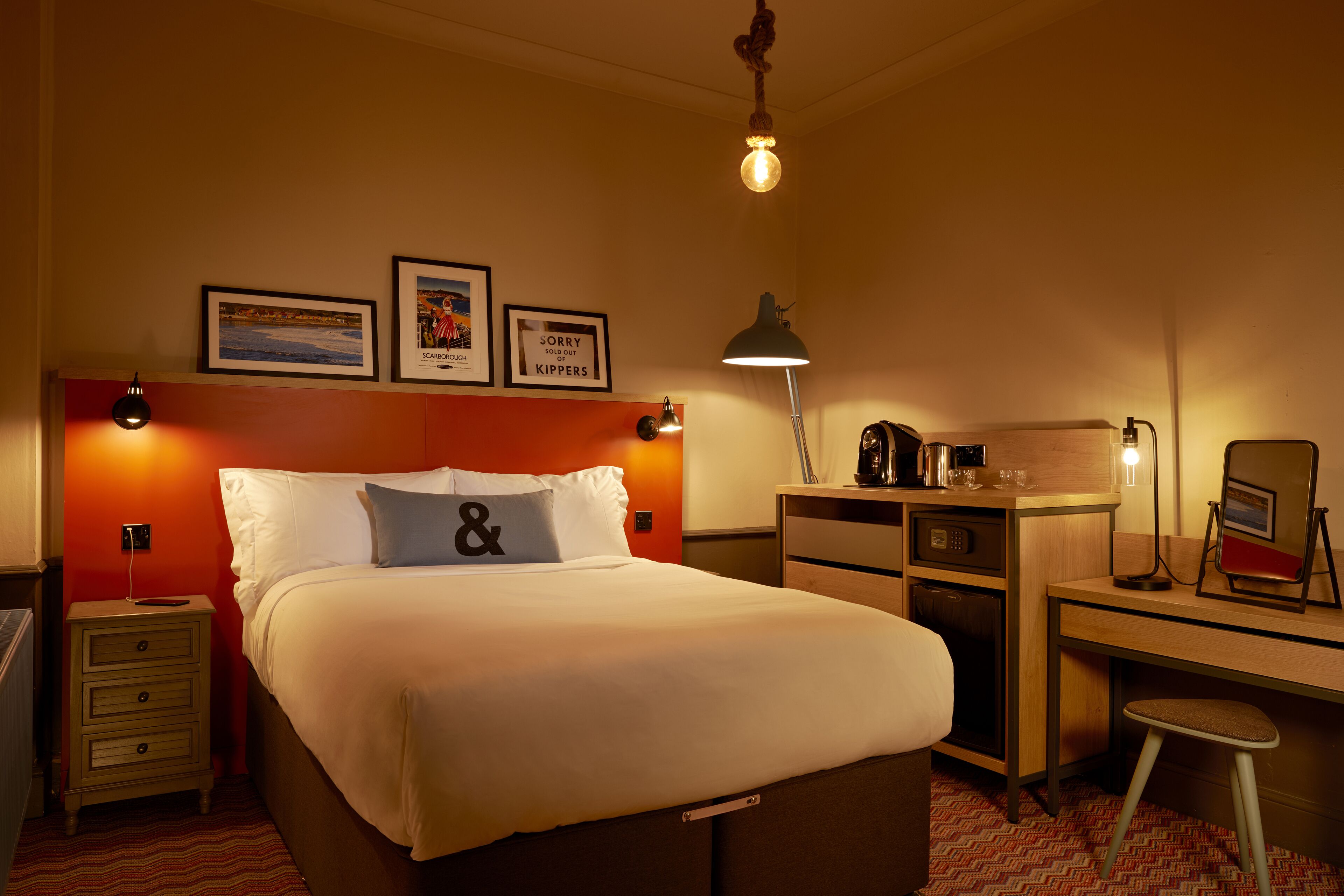 Una habitación de hotel con una cama, un escritorio, una silla, una mesita de noche y una lámpara.