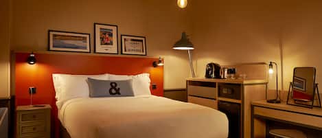 A hotel room with a bed, a desk, a chair, a nightstand, and a lamp.
