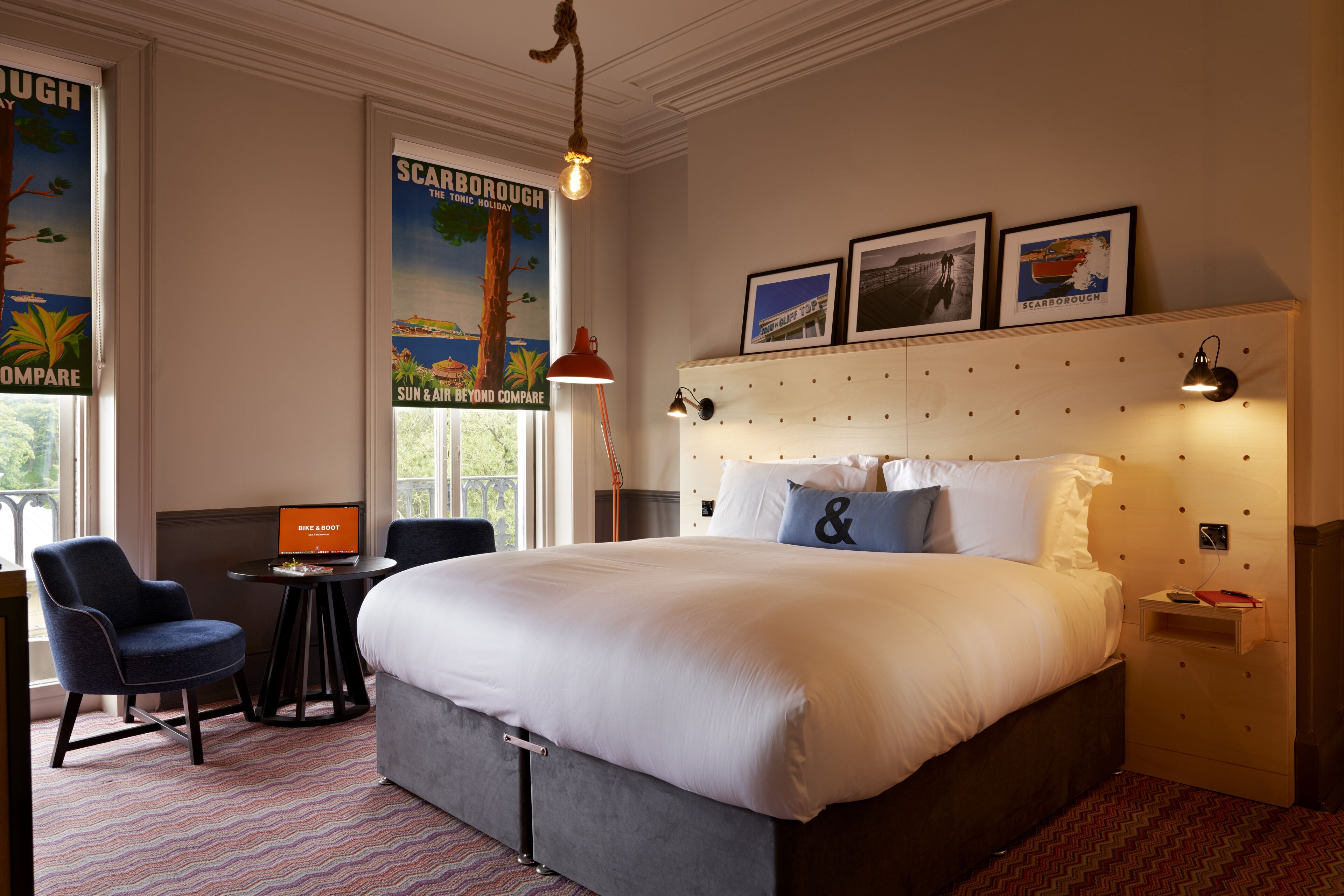 Een hotelkamer met een groot bed, een bureau met een laptop, een stoel en een poster aan de muur.