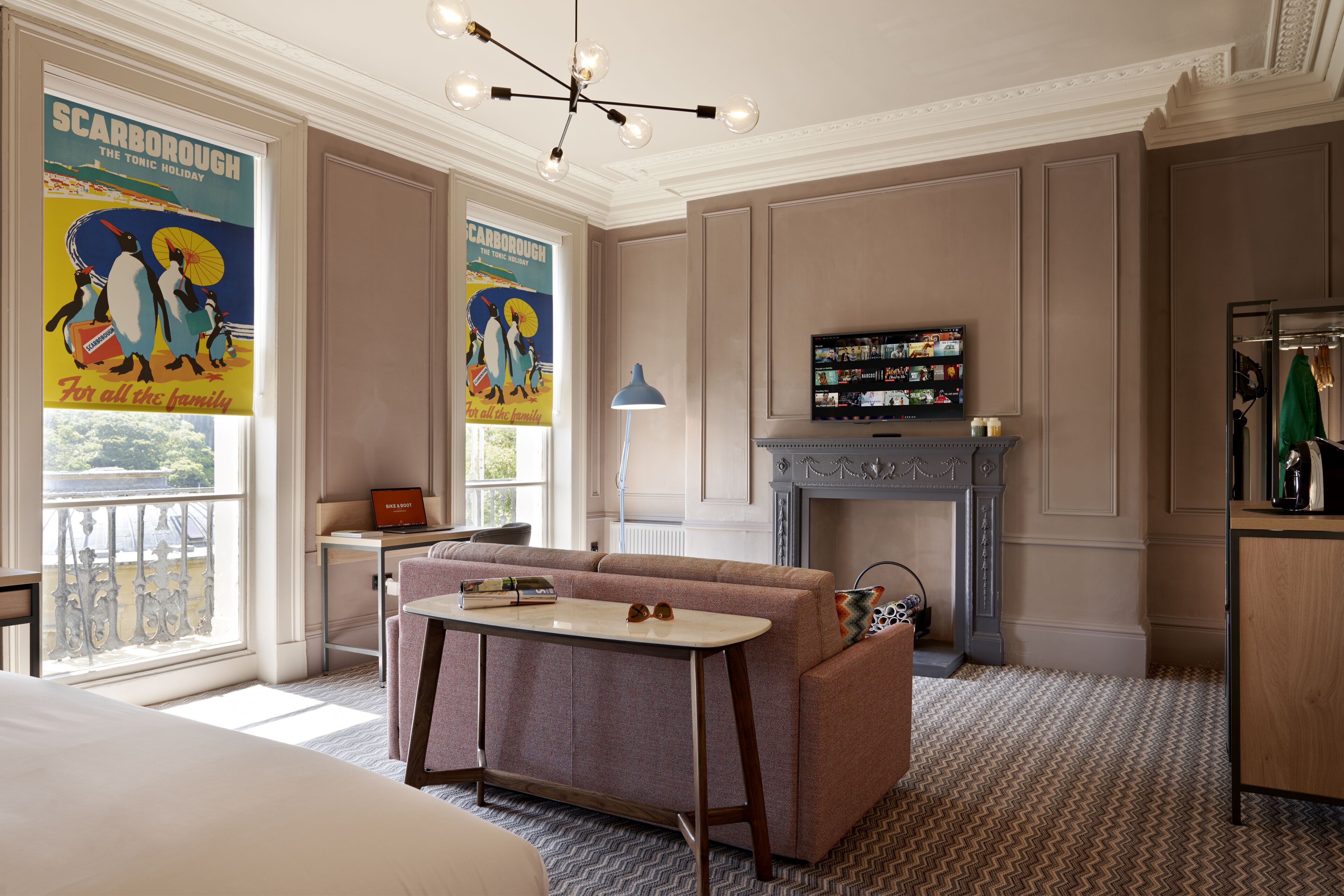 A hotel room with a large bed, a sitting area with a sofa and a small table, a television, a fireplace, and a balcony with a view.