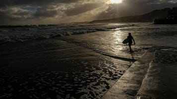 A beach scene with a person carrying a surfboard, waves, and a sunset.