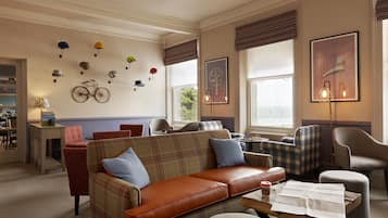 A cozy living room with a brown leather sofa, plaid-patterned armchairs, and a coffee table with a newspaper.