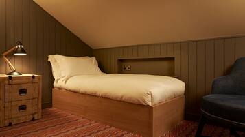 A single bed with a wooden frame, a bedside lamp, a chair, and a patterned carpet in a room with wooden paneling.
