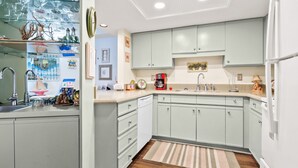 Una cocina con armarios verde claro, piso de madera, un lavamanos y una cafetera.