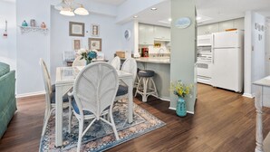Una cocina moderna con electrodomésticos blancos, una zona de comedor con sillas de mimbre y una alfombra estampada.