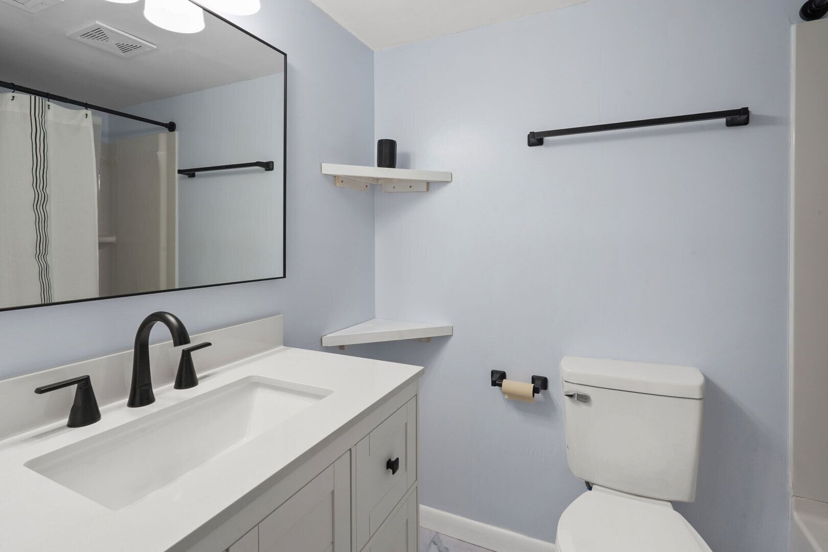 A bathroom with a white sink, black faucet, a toilet, and a mirror.