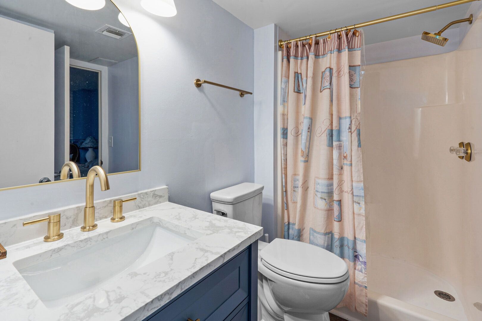 Ein Badezimmer mit Marmorwaschbecken, goldenen Armaturen, einer weißen Toilette und einem Duschvorhang mit nautischen Motiven.